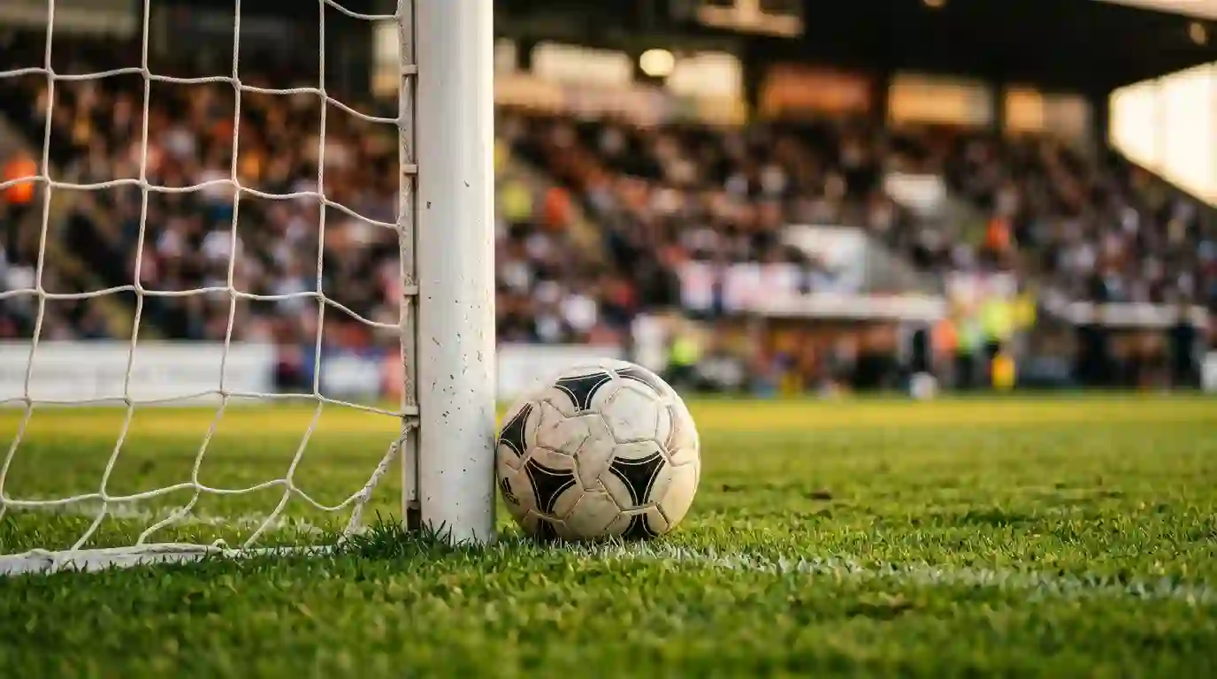 Balon de futbol junto al poste de una porteria sobre cesped verde